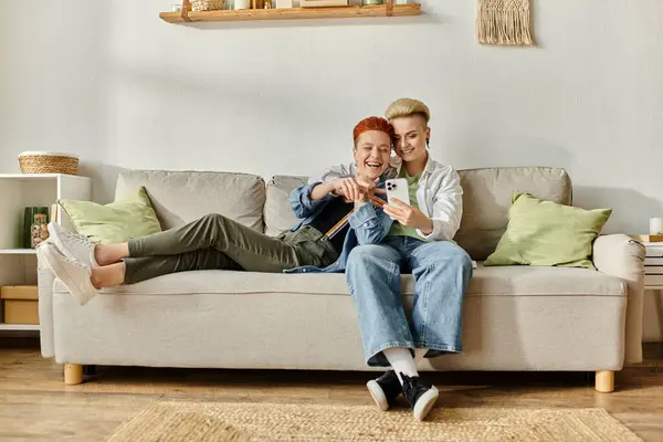 Two women, a lesbian couple with short hair, sit on a couch together in their cozy home. — Stock Photo