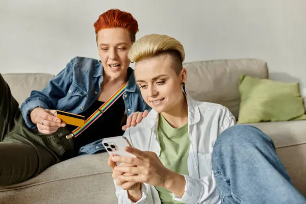 Two short-haired women sit on a couch, engrossed in a cell phones screen, sharing a moment of intimacy and connection. — Stock Photo