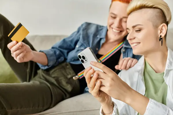 Two women with short hair, a lesbian couple, sitting on a couch, holding a credit card, discussing financial matters. — Stock Photo