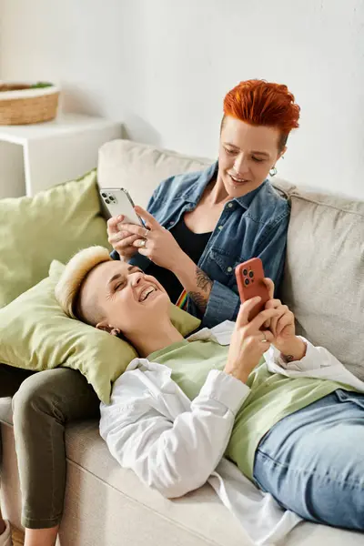 Two women, a lesbian couple with short hair, sitting on a couch engrossed in their phones. — Stock Photo