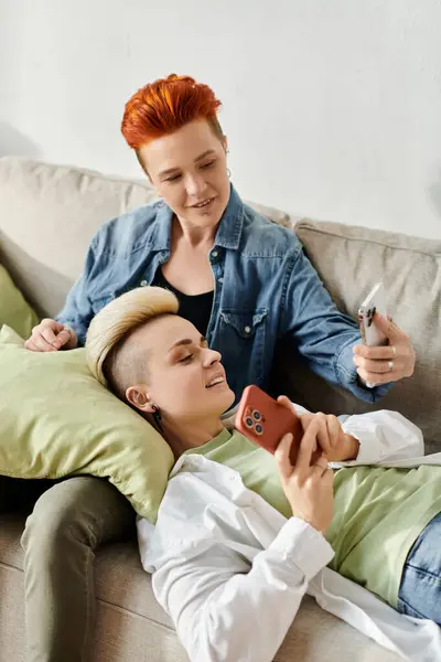 Zwei verliebte Frauen sitzen auf einer Couch, in einen gemeinsamen Moment vertieft und starren auf einen Handybildschirm.. — Stockfoto