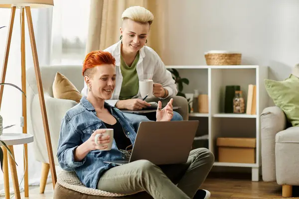 Two young women with short hair sit on a couch, engrossed in using a laptop together. — Stock Photo
