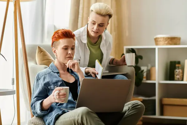Una coppia lesbica con i capelli corti che lavora su un computer portatile in un accogliente soggiorno, concentrandosi intensamente sui loro compiti. — Foto stock