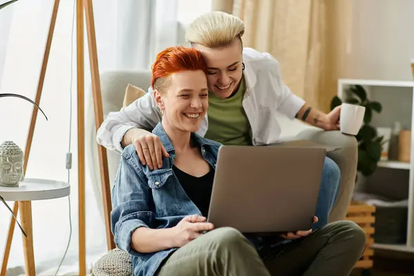 Two women, a lesbian couple, sit on a couch, engrossed in a laptop screen, sharing a quiet moment of togetherness. — Stock Photo