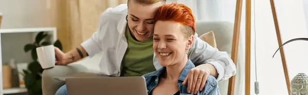 Two women with short hair sit closely together on a couch, working on a laptop. — Stock Photo