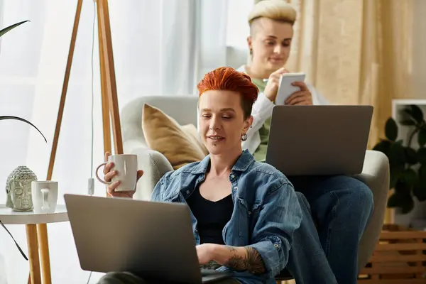 Дві жінки з коротким волоссям сидять на зручному дивані, кожен зосереджений на своїх ноутбуках, розбавлених у своєму онлайн-світі. — стокове фото