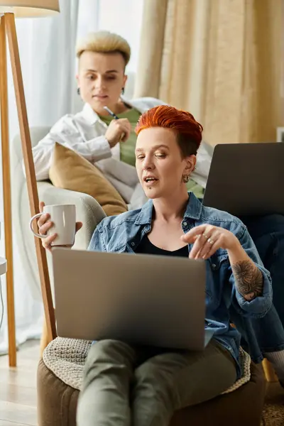 A lesbian couple with short hair comfortably sit on a couch, engrossed in using a laptop together at home. — Stock Photo
