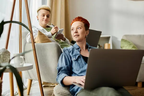 A lesbian couple with short hair sits on a couch, each engrossed in their laptop screens. — Stock Photo