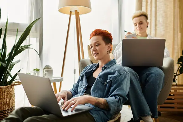 Due donne con i capelli corti, una coppia LGBT, focalizzata sui computer portatili in un ambiente elegante soggiorno. — Foto stock