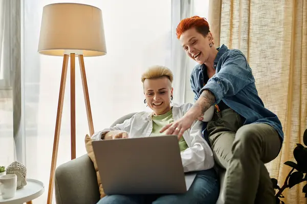 A lesbian couple with short hair sitting on a couch, focused on using a laptop together at home. — Stock Photo