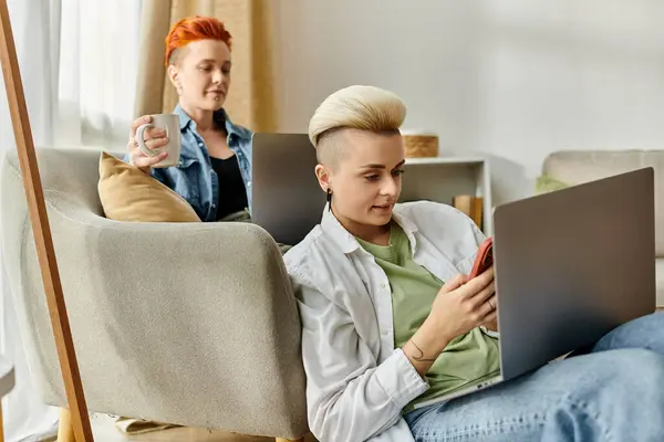 Due individui, una coppia lesbica con i capelli corti, si siedono su un divano usando i computer portatili a casa. — Foto stock