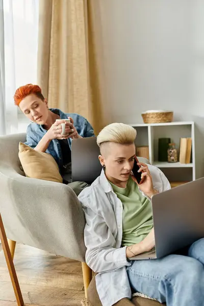 Two young men sitting closely on a couch, focused on their laptops, engrossed in their individual tasks. — Stock Photo