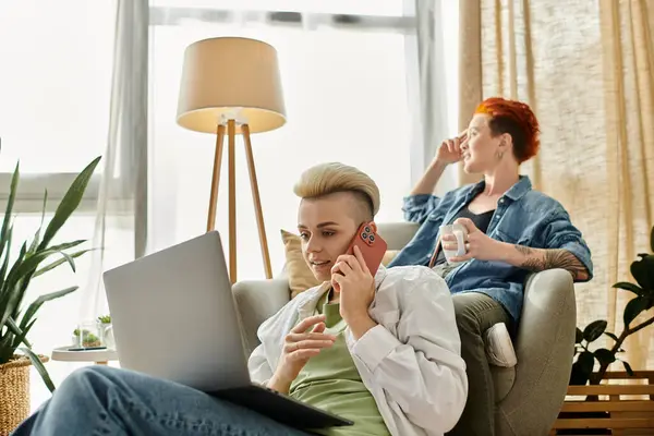 Dos personas, una pareja lesbiana con el pelo corto, están sentadas juntas en una silla, entablando una conversación profunda por teléfono. - foto de stock
