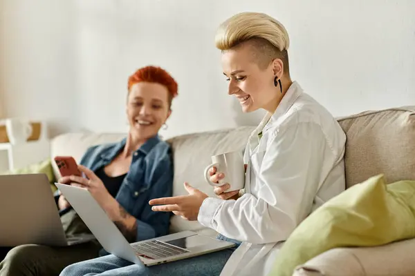 Two women, a lesbian couple with short hair, sit closely on a couch, each focused on their laptops, possibly working or sharing ideas. — Stock Photo