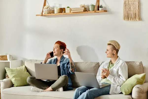 Two women, one with short hair, sitting on a couch with laptops, focused and engaged in their work or project. — Stock Photo