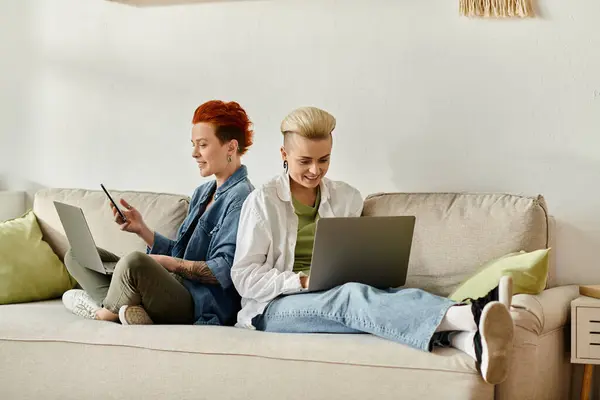 Two women with short hair sitting on a couch, engrossed in their laptops in a cozy home setting. — Stock Photo