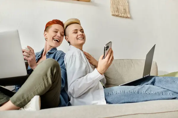 Two lgbt women with short hair studying on laptops together on a cozy couch at home. — Stock Photo