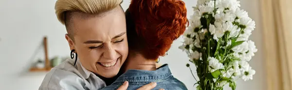 A woman with short hair lovingly hugs another woman, both holding flowers, embodying a tender moment of connection and affection. — Stock Photo