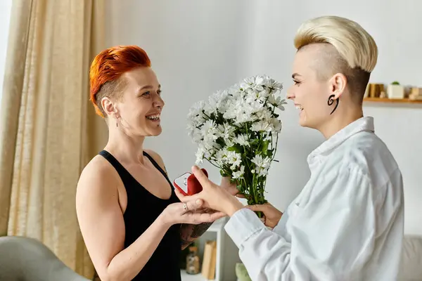 Dos mujeres con pelo corto intercambian regalos y sonrisas en una acogedora sala de estar, expresando alegría y afecto. - foto de stock