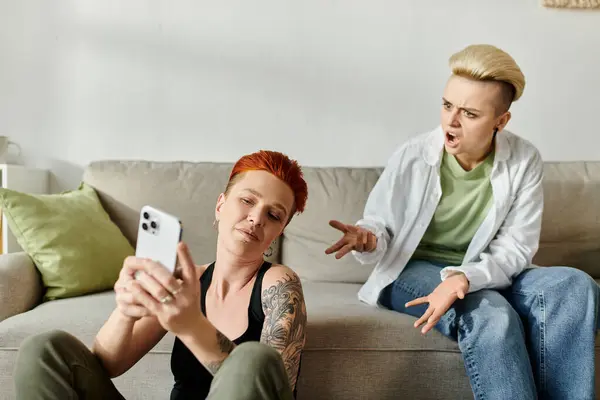 Two lgbt women sitting on a couch, engaged in browsing a cell phone together. — Stock Photo