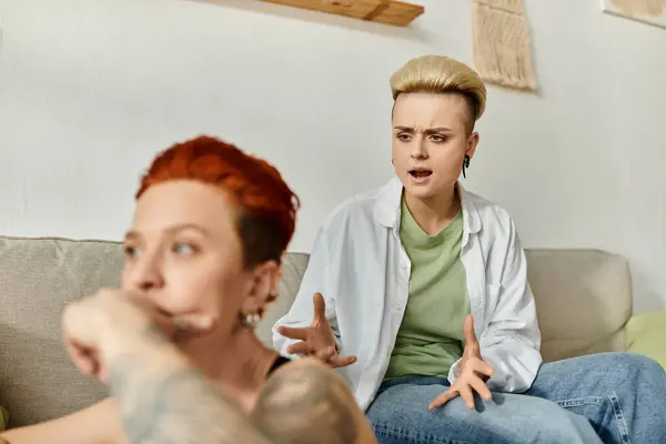 Two women with short hair sitting on a couch, engaged in emotional conversation at home. — Stock Photo