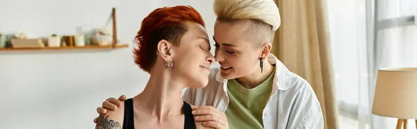 Дві жінки з коротким волоссям діляться щирими обіймами у своїй затишній вітальні, висловлюючи любов і єдність. — стокове фото