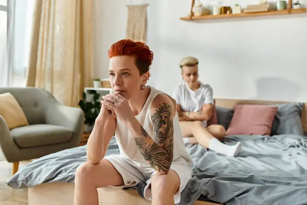 Un couple de lesbiennes aux cheveux courts assis sur un lit, mettant en valeur leurs tatouages, ayant un conflit — Photo de stock