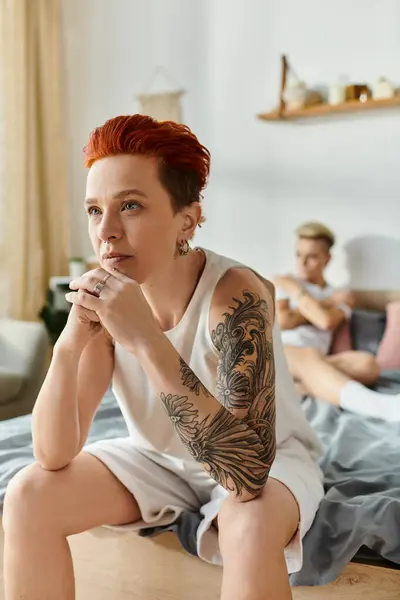 A woman with fiery red hair sits on a bed. — Stock Photo