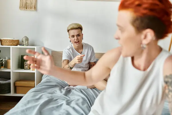 Two women, a lesbian couple with short hair, sitting on a bed, engaging in angry conversation in a bedroom setting. — Stock Photo