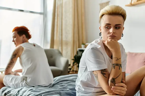 Deux femmes tatouées, un couple de lesbiennes, s'assoient ensemble sur un lit dans une chambre, mettant en valeur les difficultés relationnelles — Photo de stock