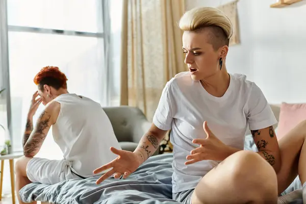 A lesbian couple, with short hair, sit on a bed engaging in emotional conversation. — Stock Photo