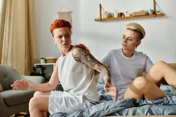 Un couple de lesbiennes avec des tatouages s'assoit étroitement sur un lit, mettant en valeur leur relation agitée dans la chambre. — Photo de stock
