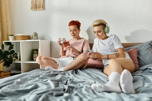 Zwei junge Frauen, ein lesbisches Paar, sitzen auf einem Bett und genießen Musik über Kopfhörer und umarmen ihre gemeinsame Liebe zur Musik.. — Stockfoto