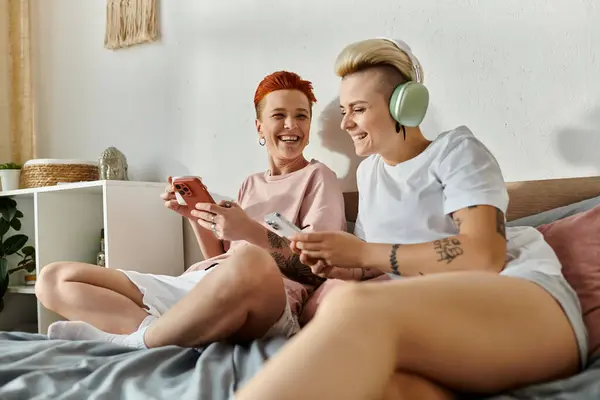 Deux femmes aux cheveux courts assises sur un lit, engagées dans des jeux ensemble, mettant en valeur un style de vie LGBT moderne. — Photo de stock
