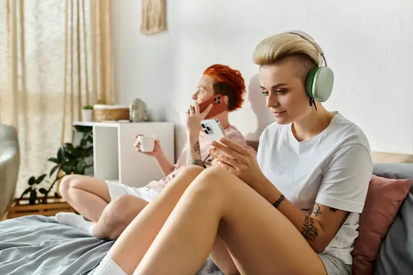 A lesbian couple with short hair sitting on a bed, engrossed in music through headphones, embodying the essence of the LGBT lifestyle. — Stock Photo