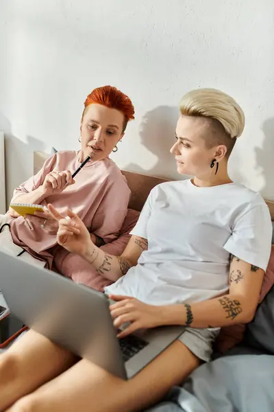 Two women, a lesbian couple with short hair, sit on a bed and engage with a laptop, embodying a modern lgbt lifestyle. — Stock Photo
