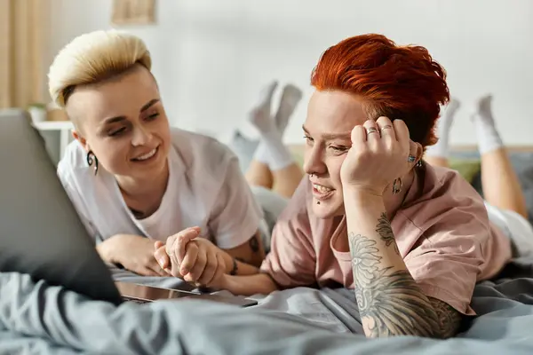 Due donne con i capelli corti si trovano su un letto, assorte in uno schermo portatile, condividendo un momento accogliente e intimo. — Foto stock