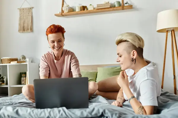 Лесбийская пара с короткими волосами наслаждается компанией друг друга на кровати во время использования ноутбука. — стоковое фото