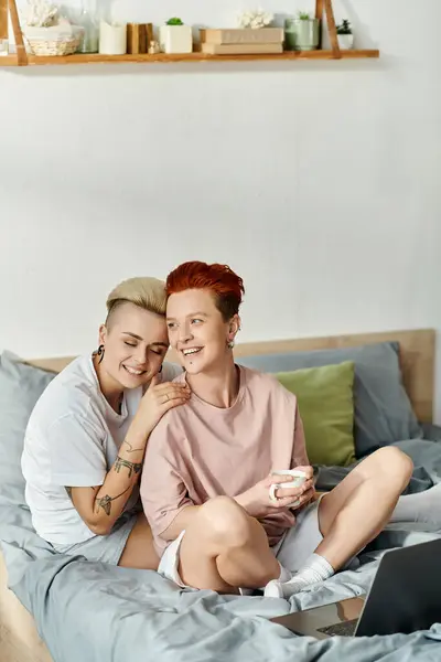 Two women, a lesbian couple, sit on a bed with laptop, focusing intently on their work in the comfort of their bedroom. — Stock Photo