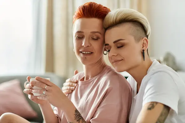Two women with short hair sit comfortably on a couch, enjoying a cup of coffee in a cozy and intimate setting. — Stock Photo