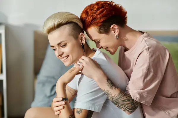 Couple lesbien aux cheveux courts serrant affectueusement sur un lit douillet dans une chambre, exprimant leur amour et embrassant leur style de vie LGBT. — Photo de stock
