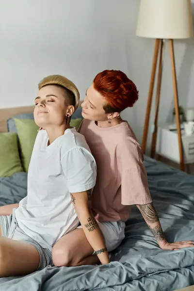 Two women, a lesbian couple, with short hair, sharing a moment on a bed adorned with tattoos, embodying the lgbt lifestyle. — Stock Photo
