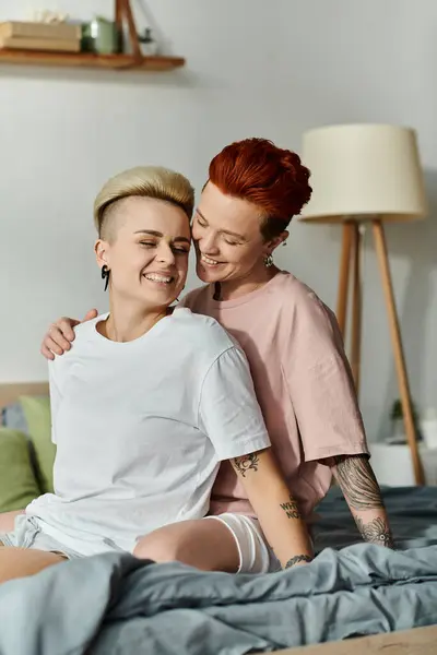 Ein warmer Moment, als zwei Menschen, ein lesbisches Paar mit kurzen Haaren, auf einem Bett sitzen und sich in ihrem Schlafzimmer umarmen. — Stockfoto