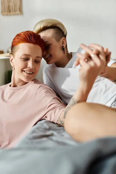 Dos mujeres con el pelo corto acostadas en una cama, compartiendo un momento alegre mientras se sonríen en un entorno íntimo. - foto de stock