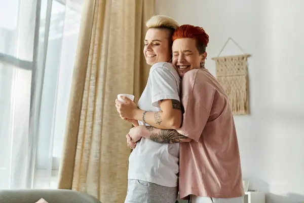 A lesbian couple with short hair hugging tenderly in front of a window, showcasing their love and closeness. — Stock Photo