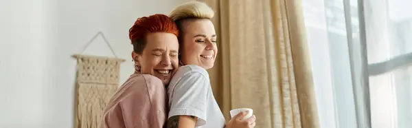 Two women with short hair embrace lovingly in front of a window, showcasing the beauty of their connection. — Stock Photo