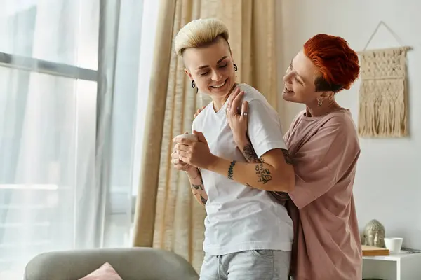 Deux femmes, un couple de lesbiennes aux cheveux courts, s'embrassent dans un salon confortable, exprimant amour et connexion. — Photo de stock