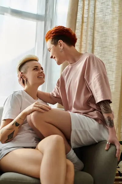 A lesbian couple with short hair sitting closely together on a comfortable couch in a cozy setting. — Stock Photo