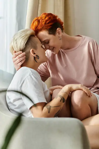 Two women with short hair cuddle affectionately on a couch in a warm and intimate setting, radiating love and warmth. — Stock Photo