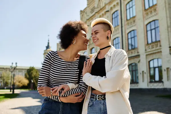 Due giovani donne alla moda si trovano con grazia di fronte a un edificio moderno in un campus universitario. — Foto stock